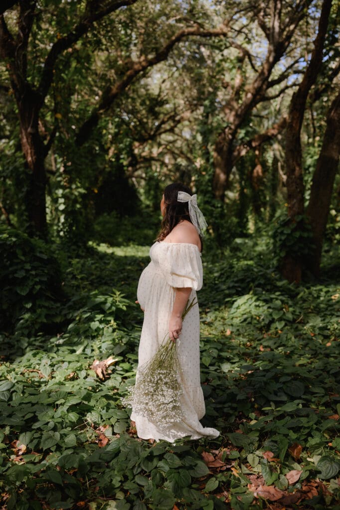 Pregnant woman in white dress standing in lush greenery at Indian Hammocks Park in Miami maternity photography session surrounded by lush greenery