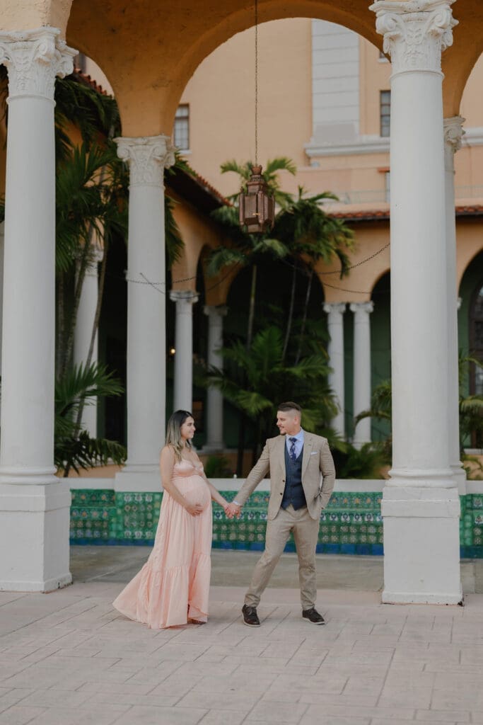 Maternity photography session at the historic Biltmore Hotel in Coral Gables with couple holding hands under Mediterranean-style archways