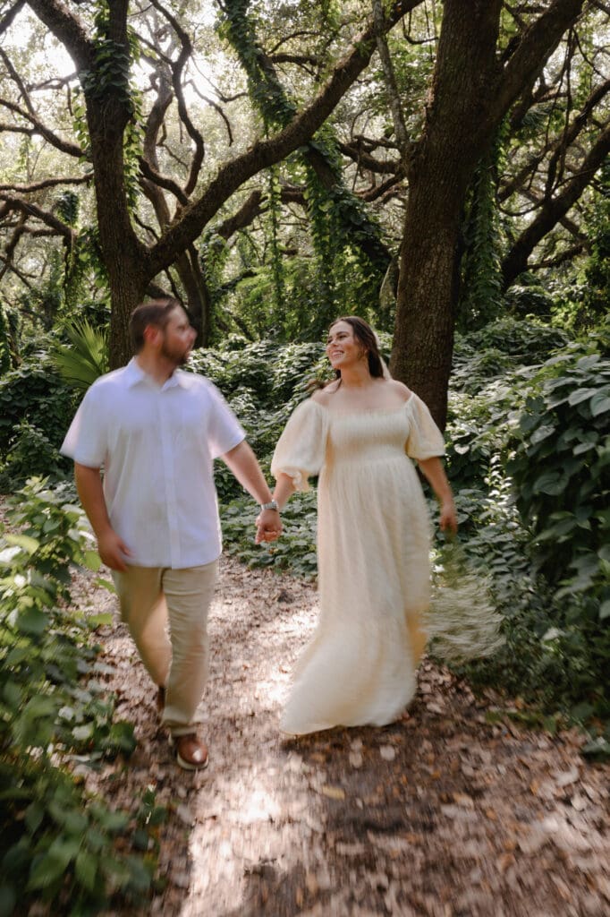 Outdoor maternity session with an expecting couple walking hand in hand along a wooded path, photographed in natural light and motion blur