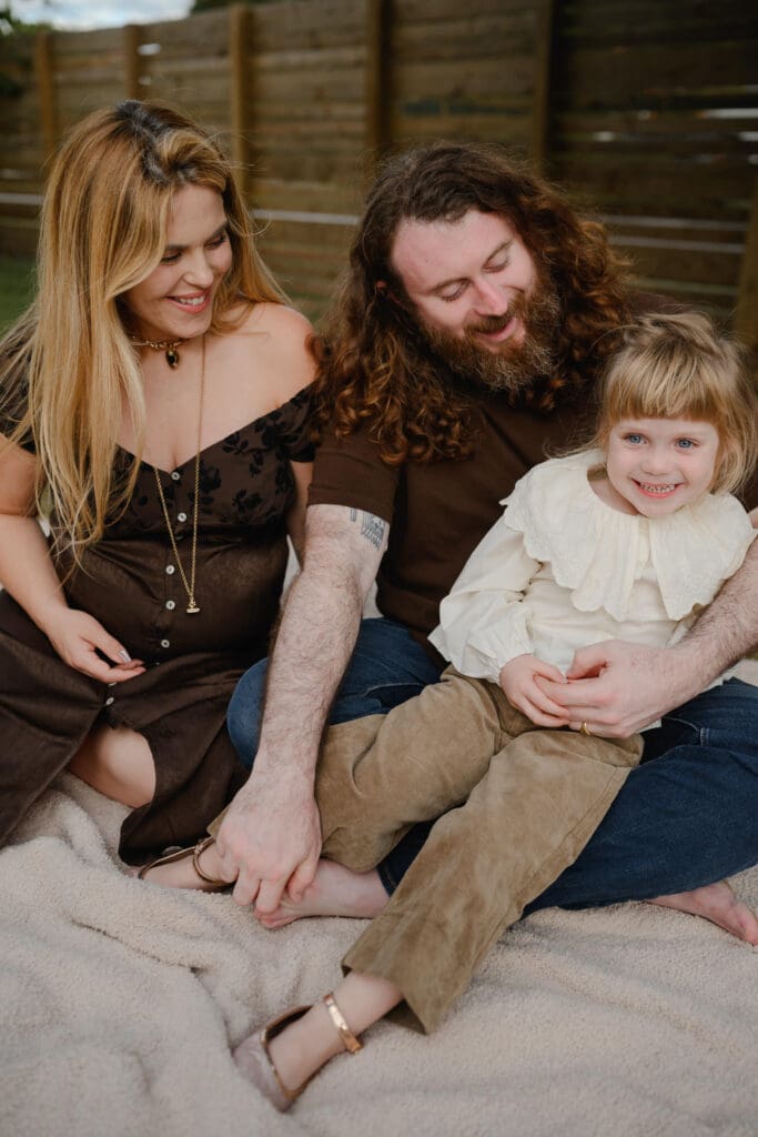 Lifestyle family photography of parents sitting with their young child on a blanket outdoors, wearing neutral clothing