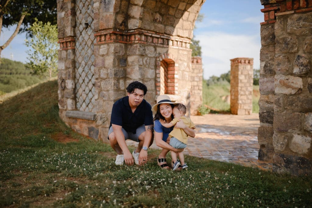Parents cuddling their toddler beneath the historic stone arch at BridgeWay Station in Greenville, South Carolina.